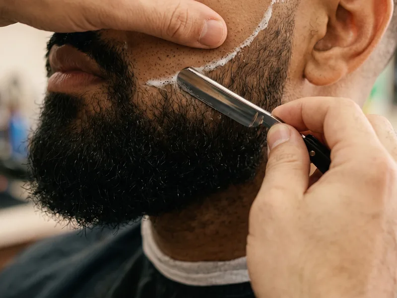 Barber shaping a beard line with a straight razor
